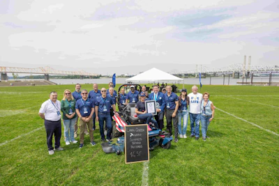 Team members celebrate world record achievement at waterfront event with tent and industrial bridges in background