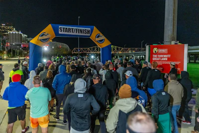 Crowd of runners gathered at a nighttime race start line with blue and yellow inflatable arch and Turfmutt event signage