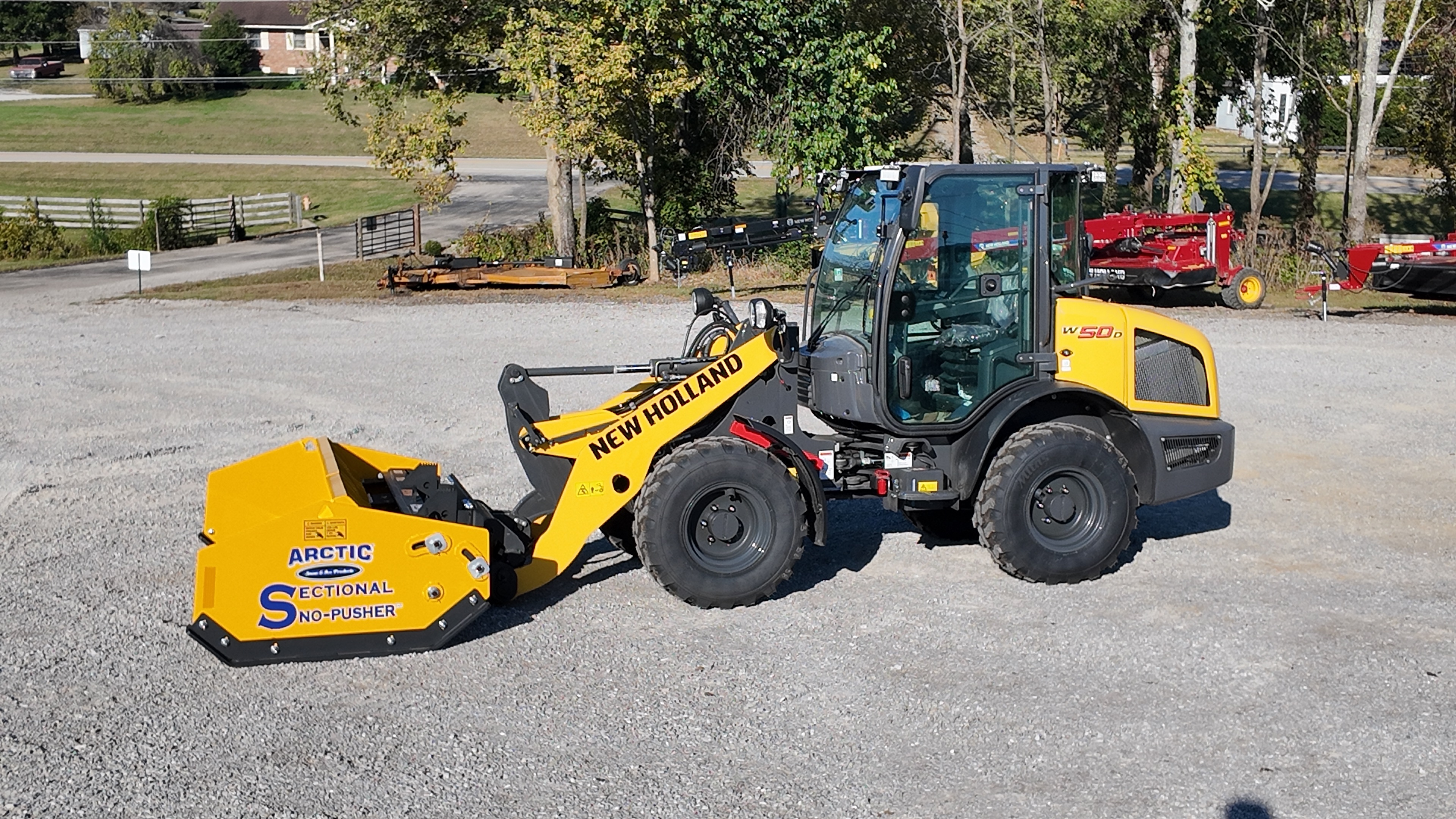 Yellow New Holland wheel loader with Arctic snow pusher attachment parked at equipment yard
