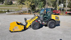 Yellow New Holland wheel loader with Arctic snow pusher attachment parked at equipment yard