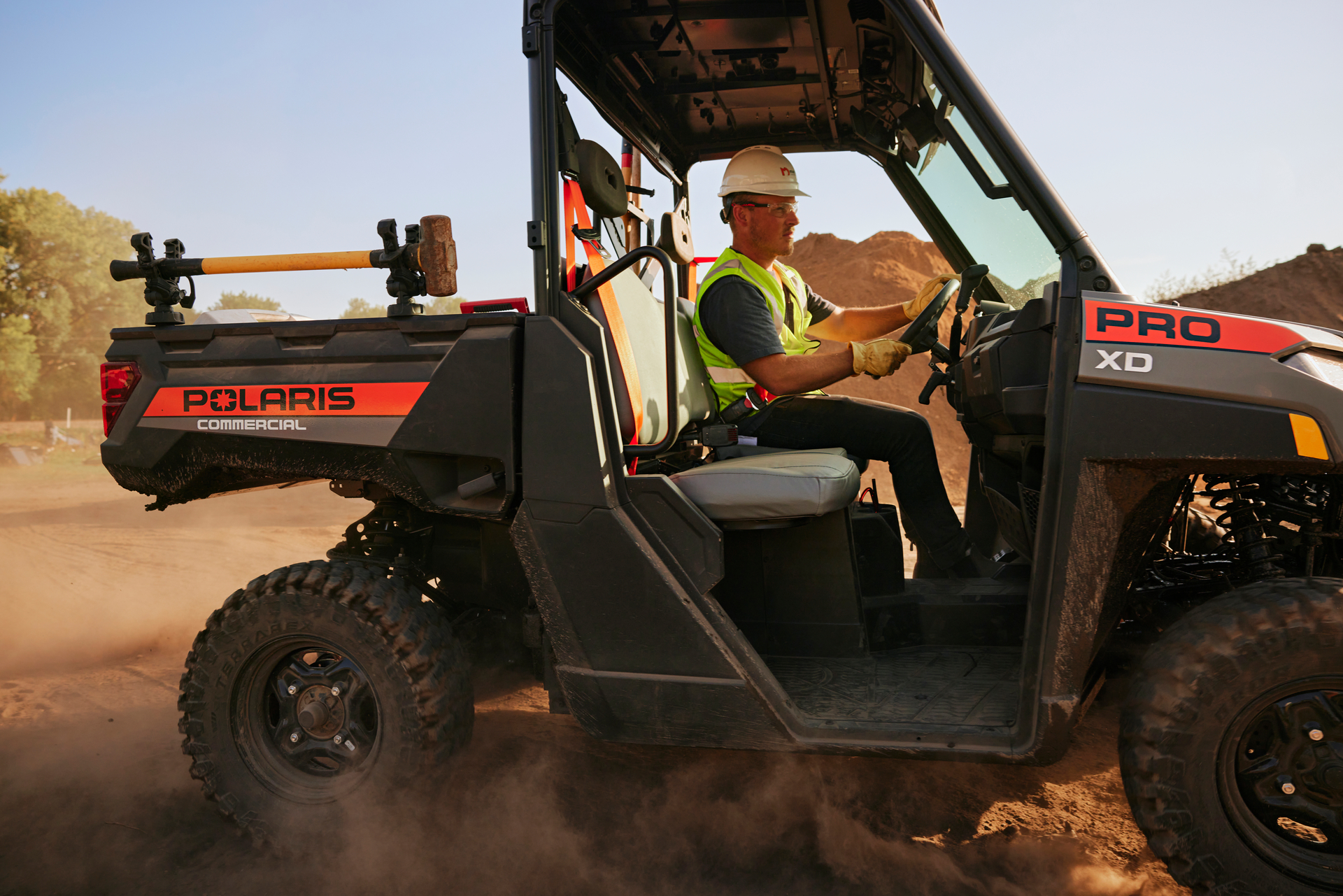 Worker operating a Polaris PRO XD commercial utility vehicle on a dusty desert terrain.