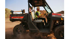 Worker operating a Polaris PRO XD commercial utility vehicle on a dusty desert terrain.