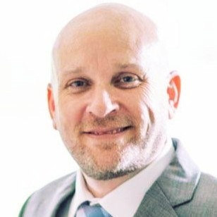 Professional headshot of a smiling man with white hair and beard wearing a gray blazer and light blue shirt Headshot